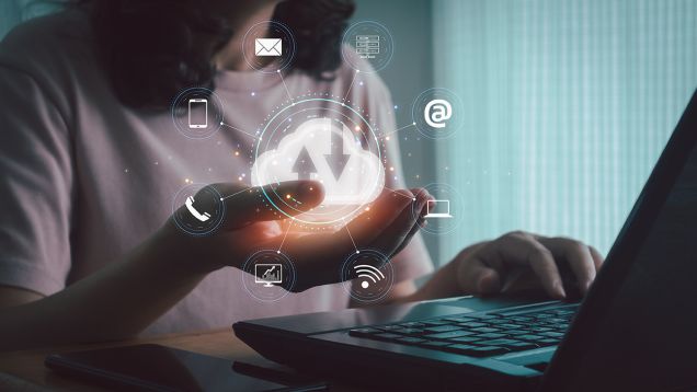 Person arbeitet am Laptop und hält eine visualisierte Cloud mit Icons für Kommunikation und Daten als Symbol für digitale Vernetzung, Cloud-Lösungen und integrierte IT-Prozesse