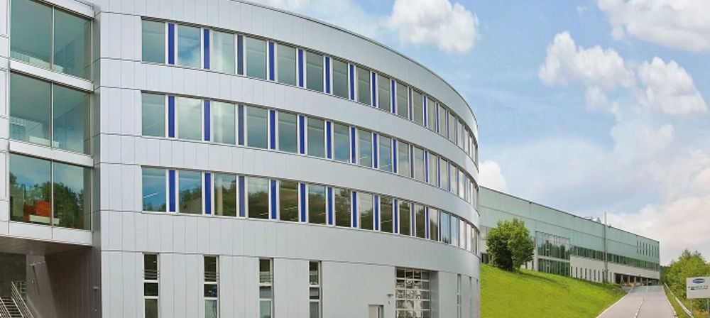 Modernes Firmengebäude mit geschwungener Fassade und Glasfront in grüner Umgebung als Symbol für zeitgemäße Architektur und Unternehmensstandort