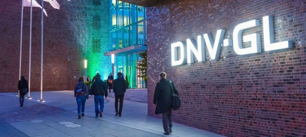 Eingangsbereich eines Gebäudes mit DNV GL Schriftzug an der Fassade und mehreren Personen auf dem Weg zum Eingang als Symbol für ein internationales Unternehmen und professionelle Geschäftsumgebung