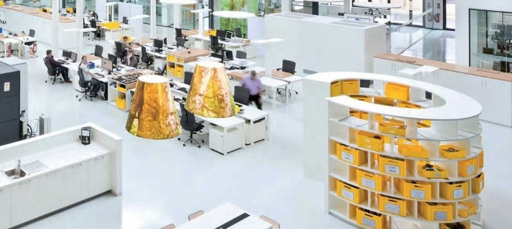Modernes, offenes Büro mit Arbeitsplätzen, Regalsystemen und Mitarbeitenden als Symbol für effiziente Arbeitsumgebung, Organisation und digitale Prozesse
