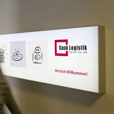 Beleuchtetes Firmenschild von Cash Logistik Security AG im Eingangsbereich mit vorbeigehender Person als Symbol für professionellen Empfang und Unternehmenspräsenz