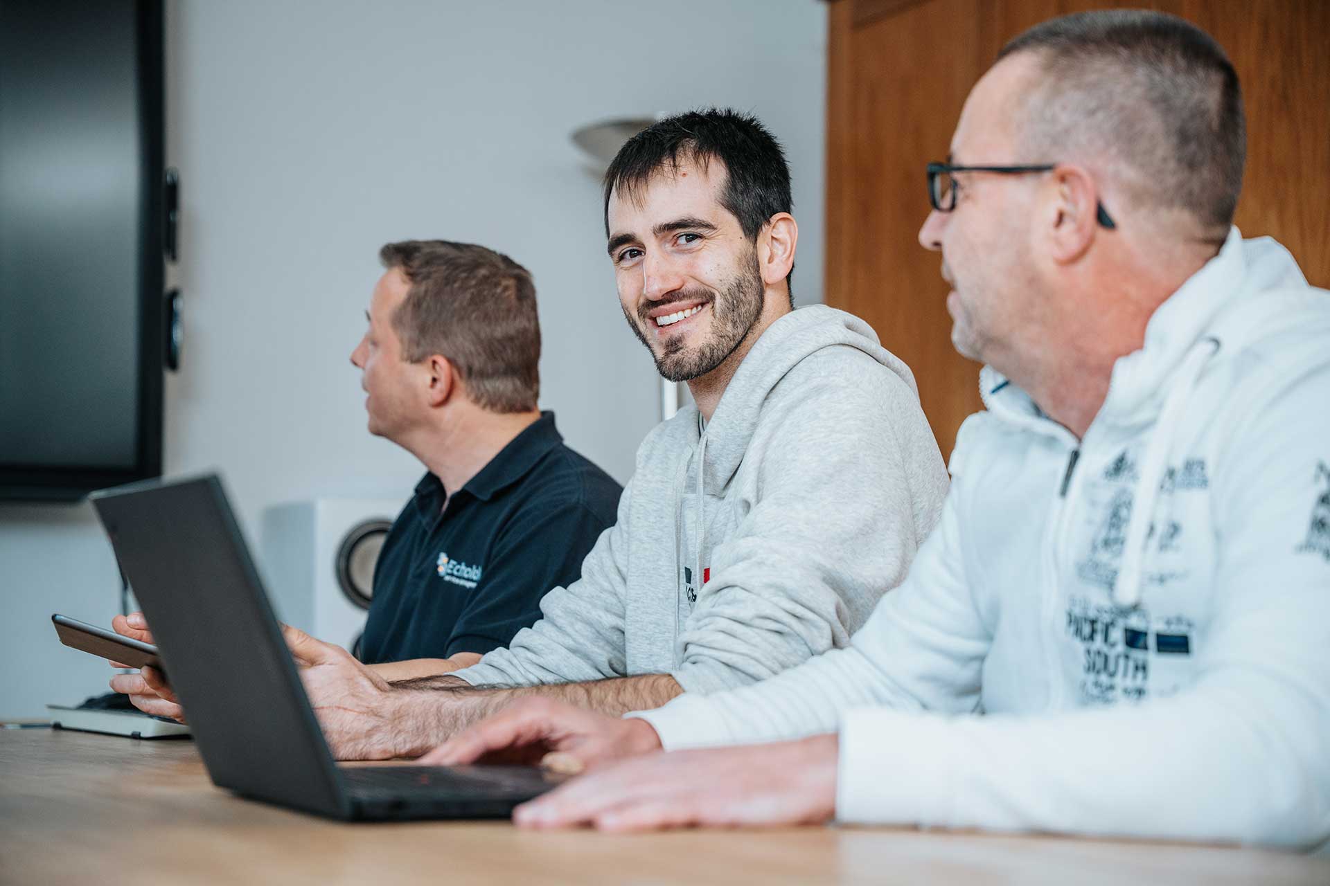 Mitarbeitende von mIT solutions arbeiten gemeinsam mit Laptop und Tablet im Meeting und stimmen sich zu digitalen Prozessen und Softwarelösungen ab