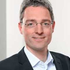 Porträt eines Mannes mit Brille im Anzug, der freundlich in die Kamera blickt und einen professionellen Eindruck vermittelt